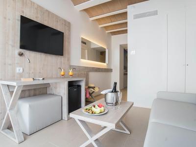 Moderní hotelový pokoj s bílým nábytkem a televizí na zdi.