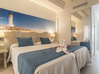 Moderní hotelový pokoj s manželskou postelí, modrobílým povlečením a nástěnnou malbou majáku.