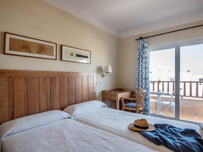 Hotelový pokoj se dvěma jednolůžky, dřevěným čelem postele, psacím stolem a balkonem s výhledem ven.