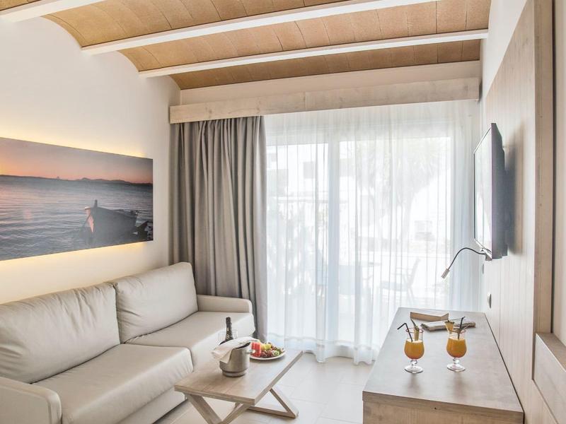 Moderní světlý obývací pokoj s dřevěnými trámy na stropě, šedou pohovkou a velkými okny se závěsy.