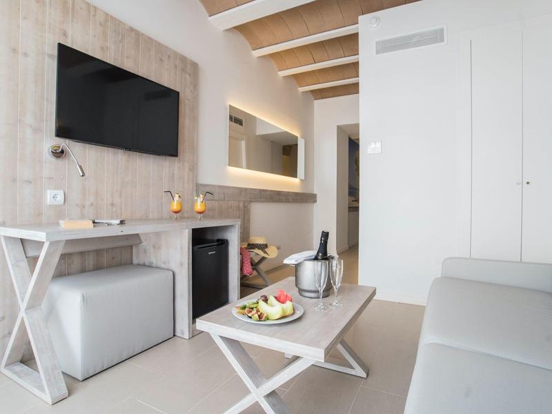 Moderní hotelový pokoj s bílým nábytkem a televizí na zdi.