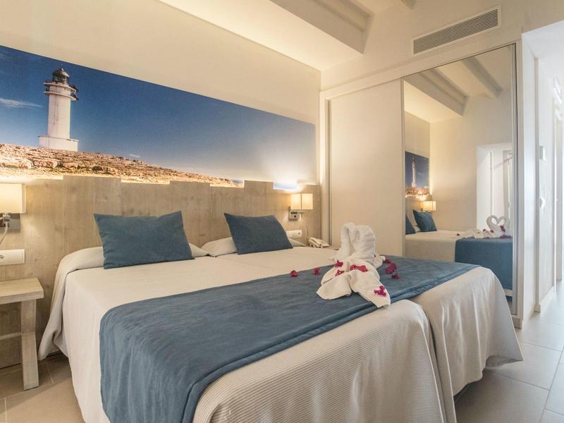 Moderní hotelový pokoj s manželskou postelí, modrobílým povlečením a nástěnnou malbou majáku.