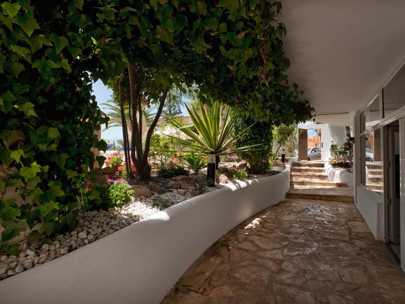 Ein heller, überdachter Gang mit Pflanzen, weißen Steinmauern und steinigem Bodenbelag.