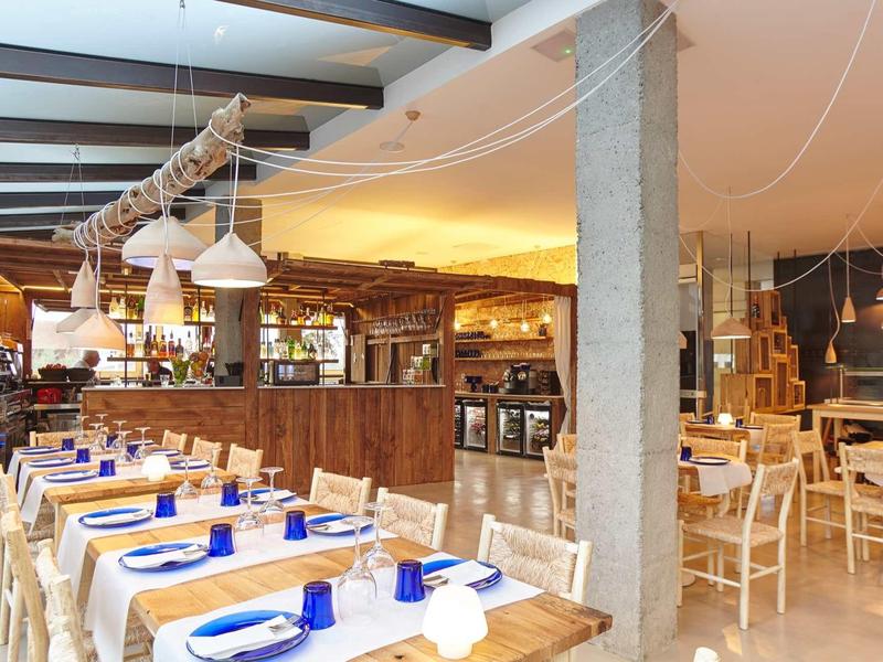 Hell beleuchteter, rustikaler Gastraum mit Holzmöbeln, blauen Gläsern und weißen Servietten.