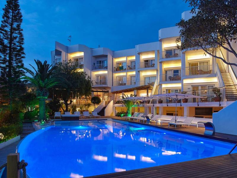 Modernes Hotelgebäude mit beleuchtetem Pool und Palmen bei Dämmerung.