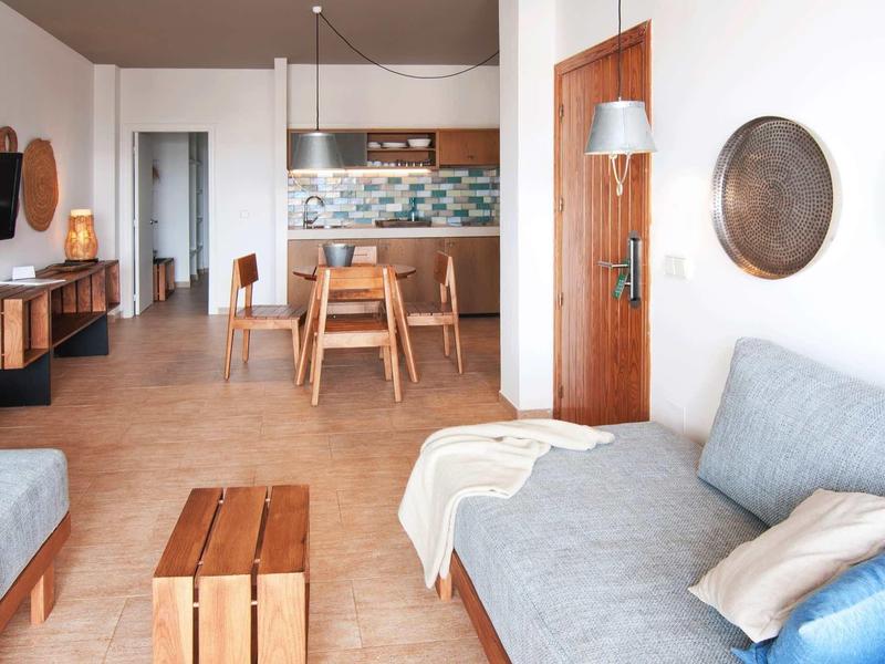 Moderner Wohnbereich mit grauen Sofas, Holzmöbeln, Esstisch und offener Küche in hellem Design.