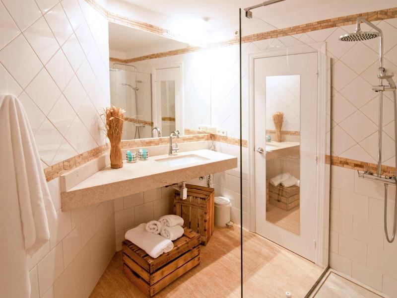 Helles Badezimmer mit Glasdusche, großem Spiegel, Holzablage, Handtüchern und weißer Wandfliese.