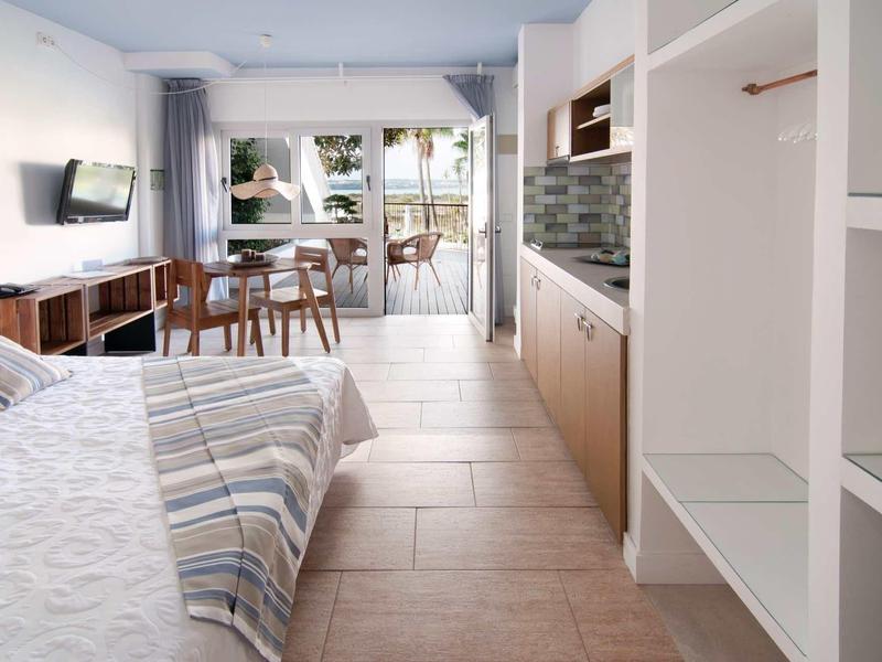 Modernes Schlafzimmer mit Bett, Holzregal, Fernseher und großem Fenster mit Blick nach draußen.