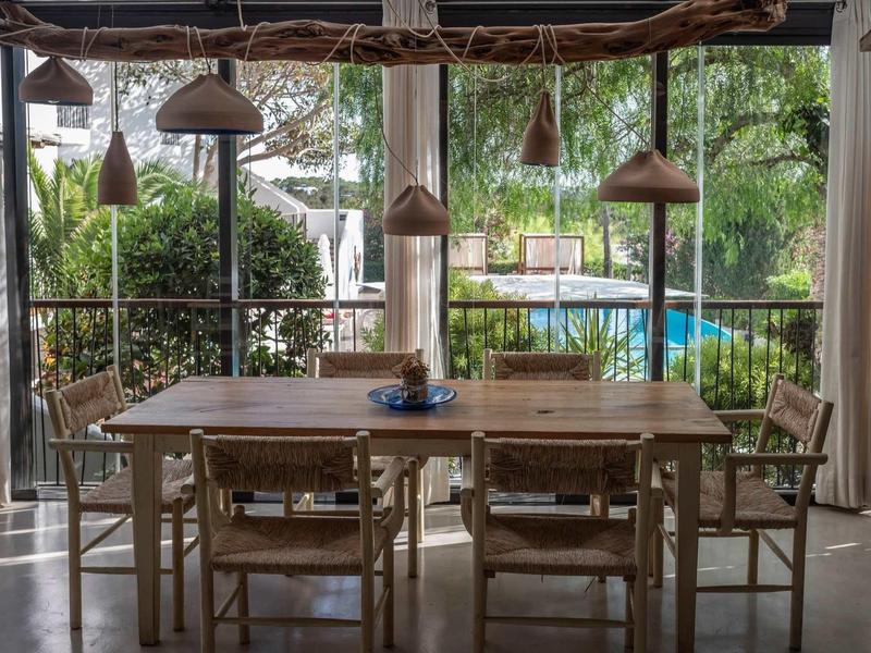 Esszimmer mit Holztisch und sechs Stühlen, großer Fensterblick auf Garten und Pool.