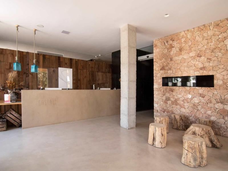 Moderner Empfangsbereich mit Steinwänden, Holzdetails, Betonboden und hängenden blauen Lampen.