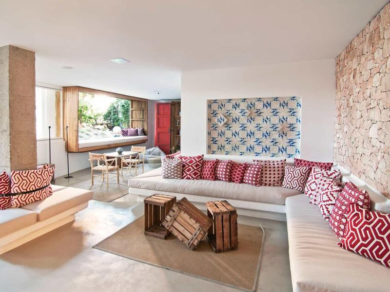 Helle Wohnzimmer mit Steinwand, weißem Ecksofa, gemusterten Kissen und Holz-Lounge-Stühlen.