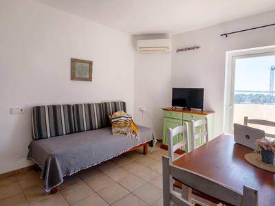 Heller Raum mit Sofa, TV, Esstisch und Blick auf das Meer durch die Tür