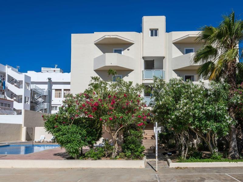 Modern hotel building with balconies surrounded by trees under a blue sky.