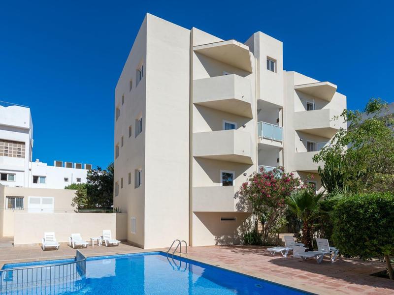 Multi-story apartment building with pool and lounge chairs on a sunny day.