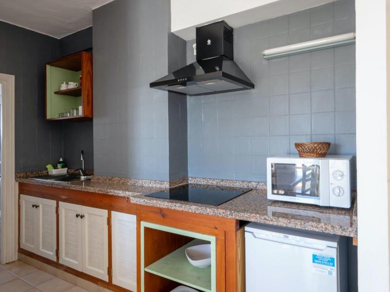 Modern kitchenette with stovetop, extractor hood, microwave, and open shelf