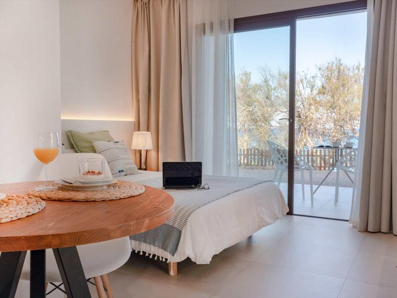 Helles Schlafzimmer mit Bett, rundem Holztisch, Fenster zur Terrasse und sanften Vorhängen.