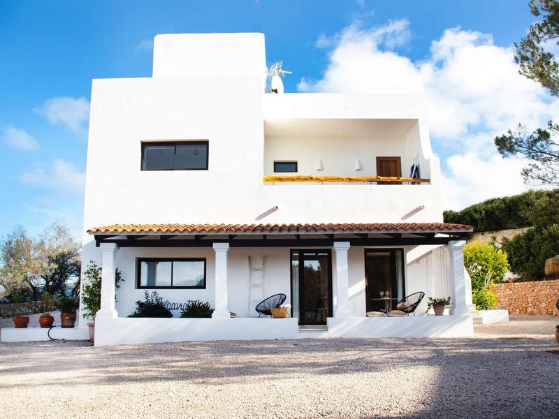 Zwei Stockwerke großes weißes Haus mit Flachdach, braunen Holzakzenten und blauem Himmel.