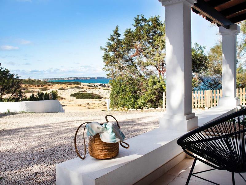 Terrasse mit weißen Säulen, schwarzem Stuhl und Blick auf Garten, Bäume und blauen Himmel.