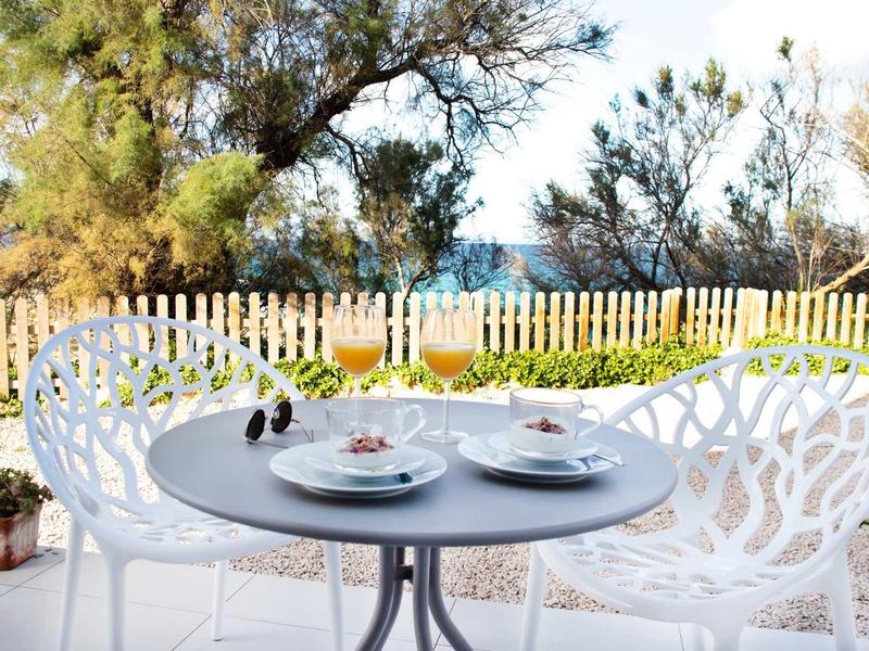 Runder Gartentisch mit zwei weißen Stühlen, gedeckt mit Gläsern, Tellern und rotem Wein, helles Licht.