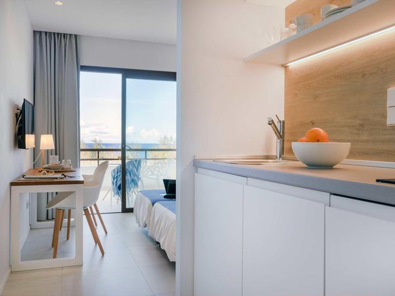 Helle Wohnung mit moderner Küche, Holzarbeitsplatte, weißem Mobiliar und Balkon mit Meerblick.