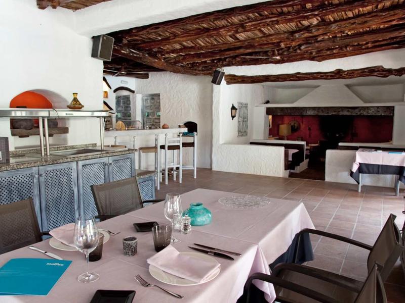Rustykalna restauracja z drewnianym sufitem z belek i nakrytymi stołami w jasnym pomieszczeniu.