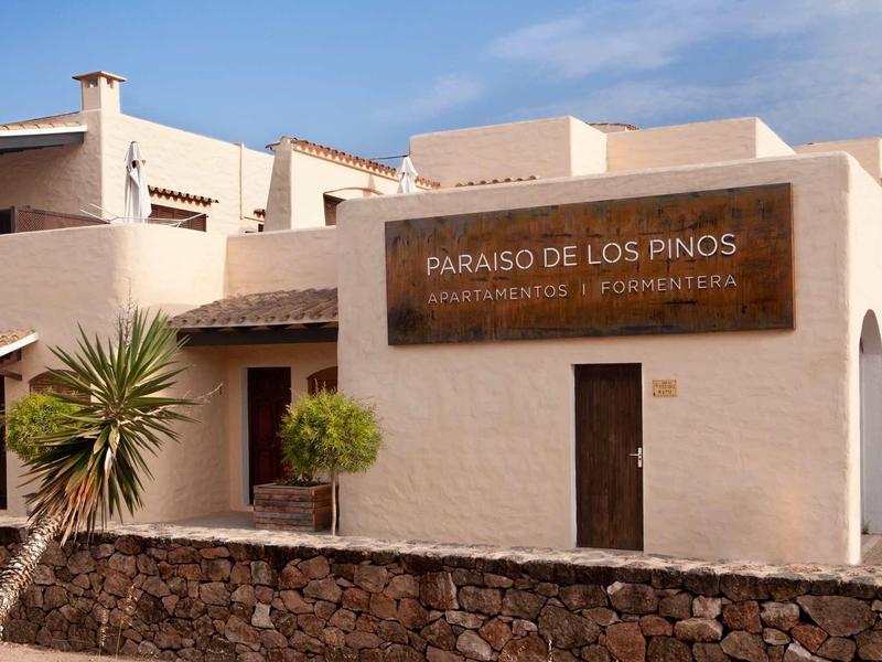 Biały budynek z tablicą 'Paraiso de los Pianos' pod niebieskim niebem w słonecznym miejscu wakacyjnym.