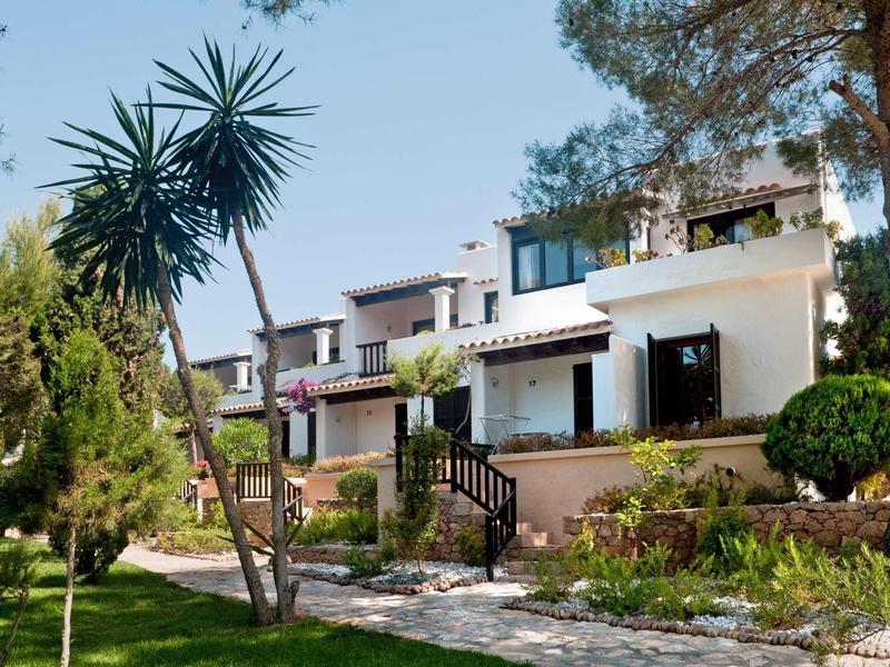 Nowoczesne białe apartamenty wakacyjne z tarasami, otoczone drzewami i zadbanym ogrodem.