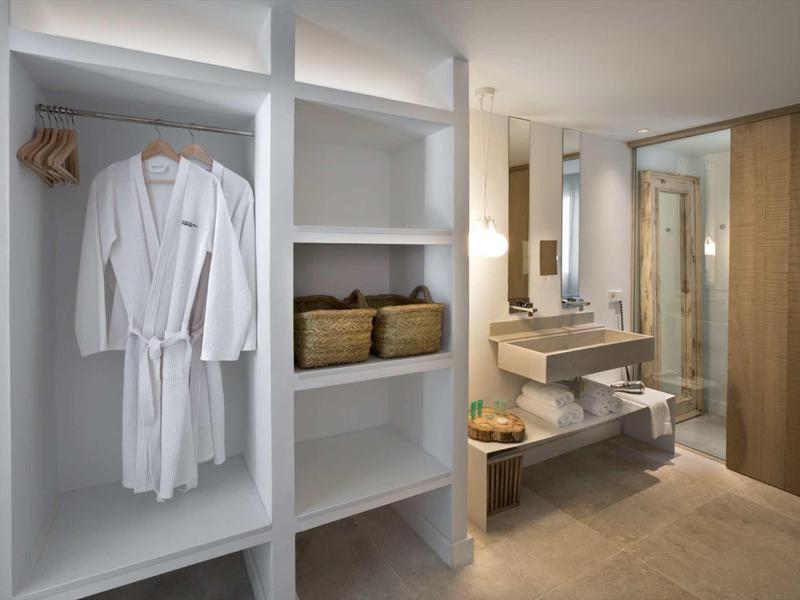 Nowoczesna łazienka hotelowa z otwartą garderobą, szlafrokiem, umywalką i prysznicem typu walk-in.