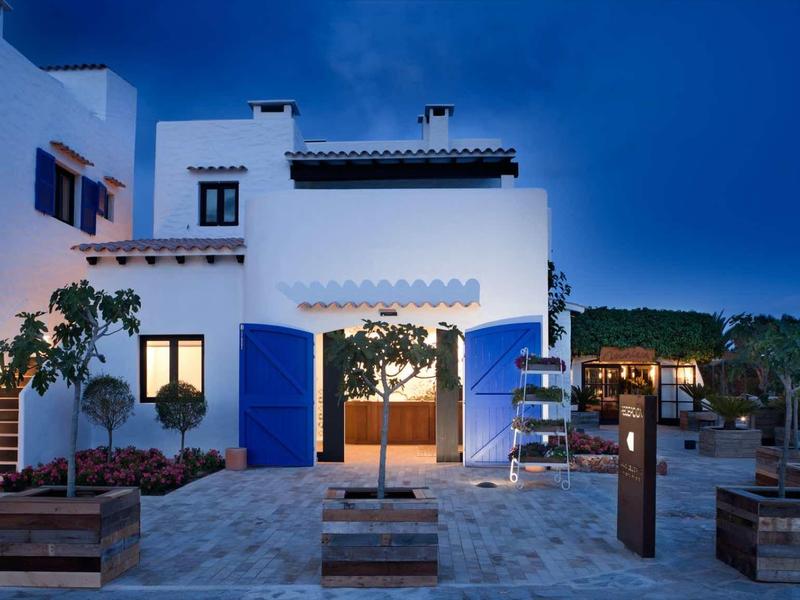 Nowoczesny biało-niebieski budynek hotelu z przytulnie oświetlonym terenem na zewnątrz o zmierzchu.