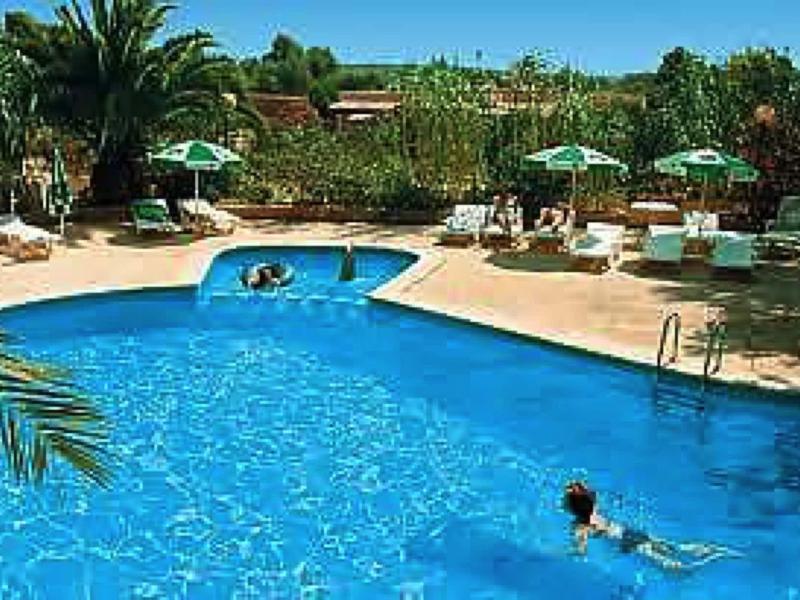A hotel pool with two people swimming and lounge chairs under green umbrellas.