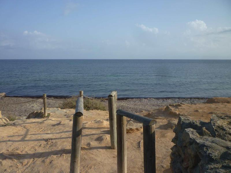 Sandy beach with simple wooden fence and calm sea in the background.