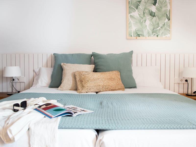 Przytulne podwójne łóżko z niebieskim narzutem, poduszkami i dekoracją ścienną w nowoczesnej sypialni.