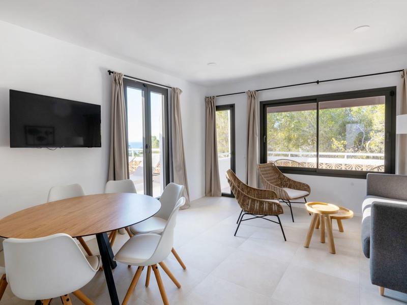 Jasny salon z stołem jadalnym, białymi krzesłami, sofą i dużymi oknami z widokiem.