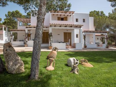 Bungalow moderno blanco con césped, árboles y objetos artísticos en primer plano.