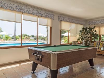 Ein Tisch mit Poolbillard in einem hellen Raum mit großen Fenstern und Blick auf einen Pool.