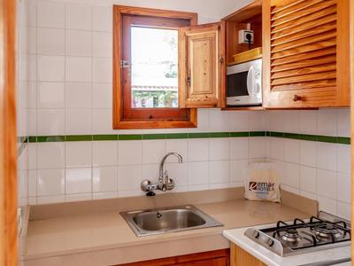 Pequeña cocina con fregadero, estufa de gas, armarios de madera y ventana abierta.