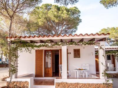 Pequeña casa de vacaciones con terraza, muebles blancos y rodeada de árboles
