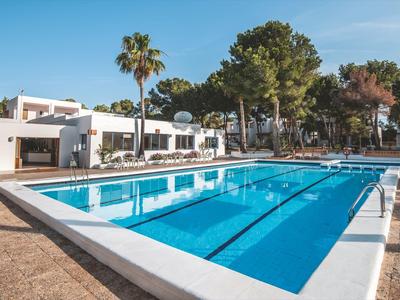 Piscina exterior moderna con tumbonas blancas y palmeras en el jardín de un hotel.