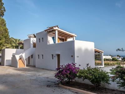 Casa de vacaciones blanca con terraza rodeada de plantas bajo un cielo azul claro.
