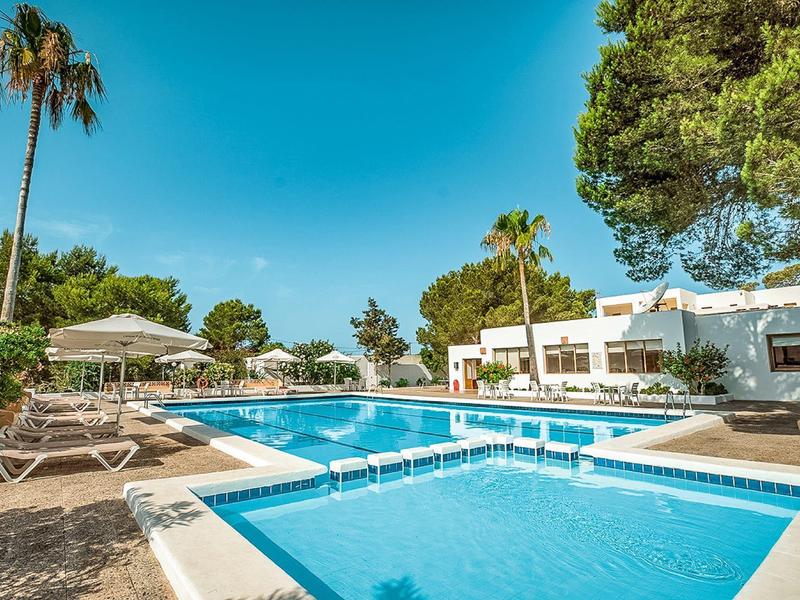 Gran piscina de hotel con tumbonas, palmeras y edificio blanco bajo cielo despejado.
