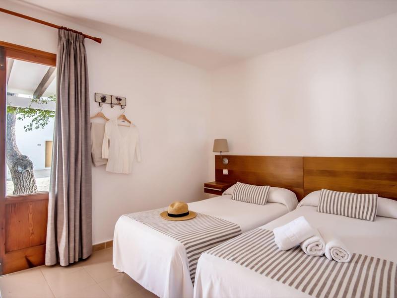 Una habitación de hotel luminosa con dos camas individuales, puerta de madera, cortinas y decoración minimalista.