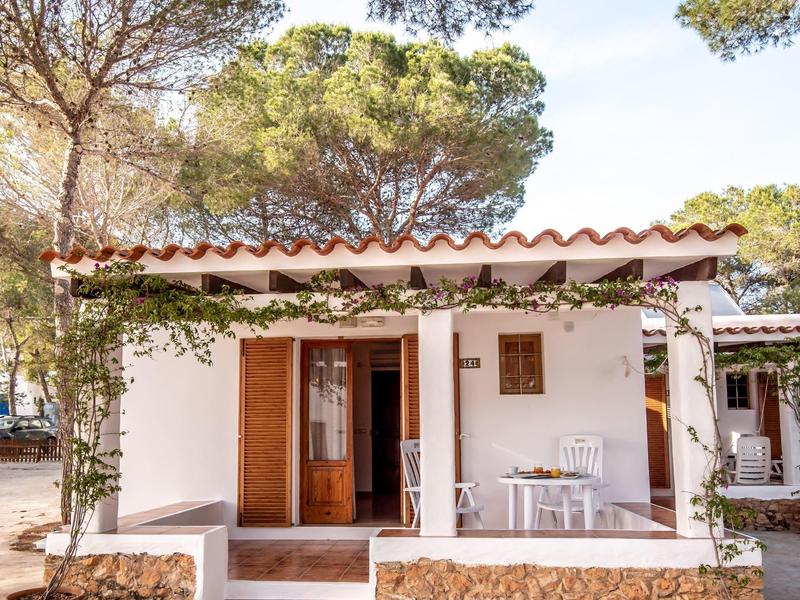 Pequeña casa de vacaciones con terraza, muebles blancos y rodeada de árboles