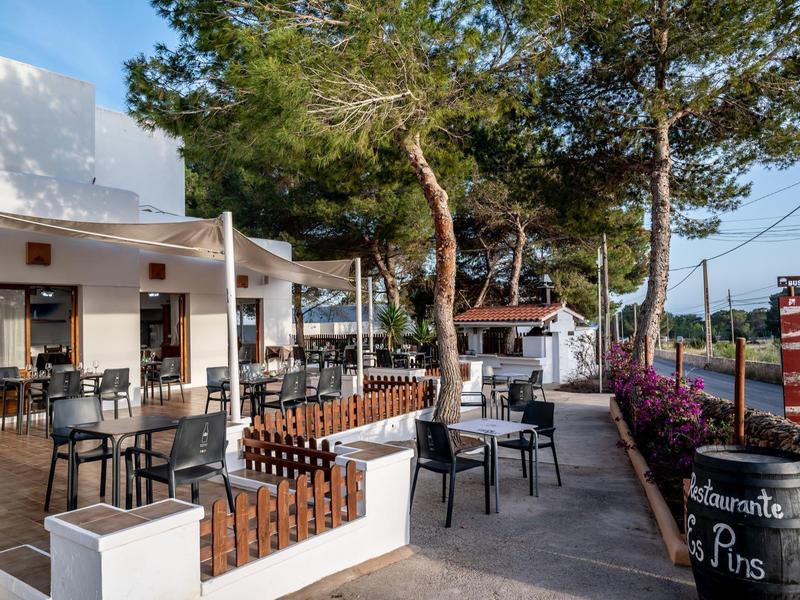 Área moderna al aire libre de un café con asientos y árboles al fondo.