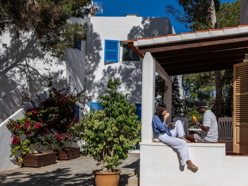 Dos personas bajo un área al aire libre cubierta junto a un edificio blanco con contraventanas azules.
