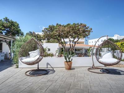 Two hanging wicker chairs on a patio with a tree and clear blue sky.