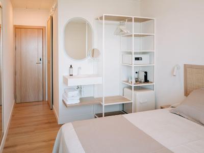 Modernes Hotelzimmer mit Bett, offenem Regal, Spiegel und Holztür im Flur.