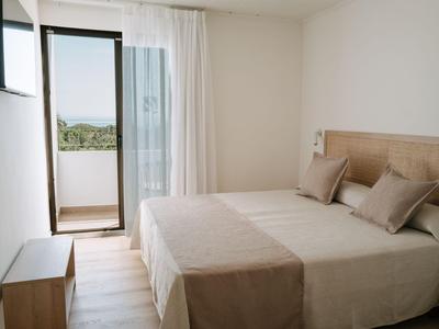 Helles Hotelzimmer mit Doppelbett, Holzmöbeln und offenem Balkon mit Blick ins Grüne.