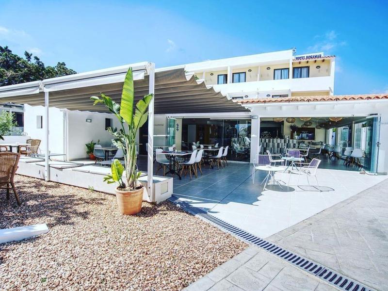 Modern hotel outdoor area with seating, plant, and sunshade under clear sky.