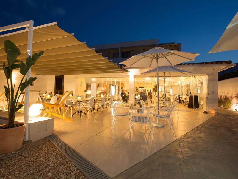 Illuminated hotel terrace with tables, chairs, and umbrellas at dusk.