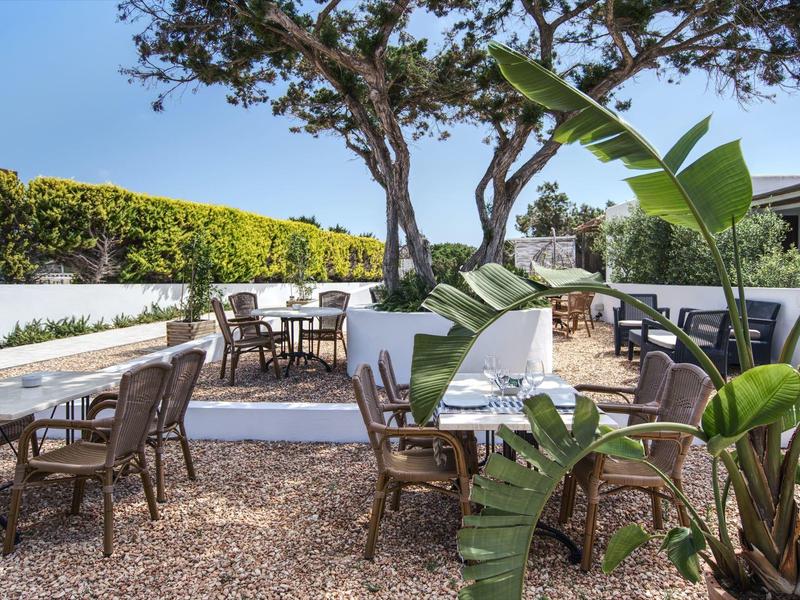 Outdoor seating area of a hotel with tables, chairs, and plants under a blue sky.